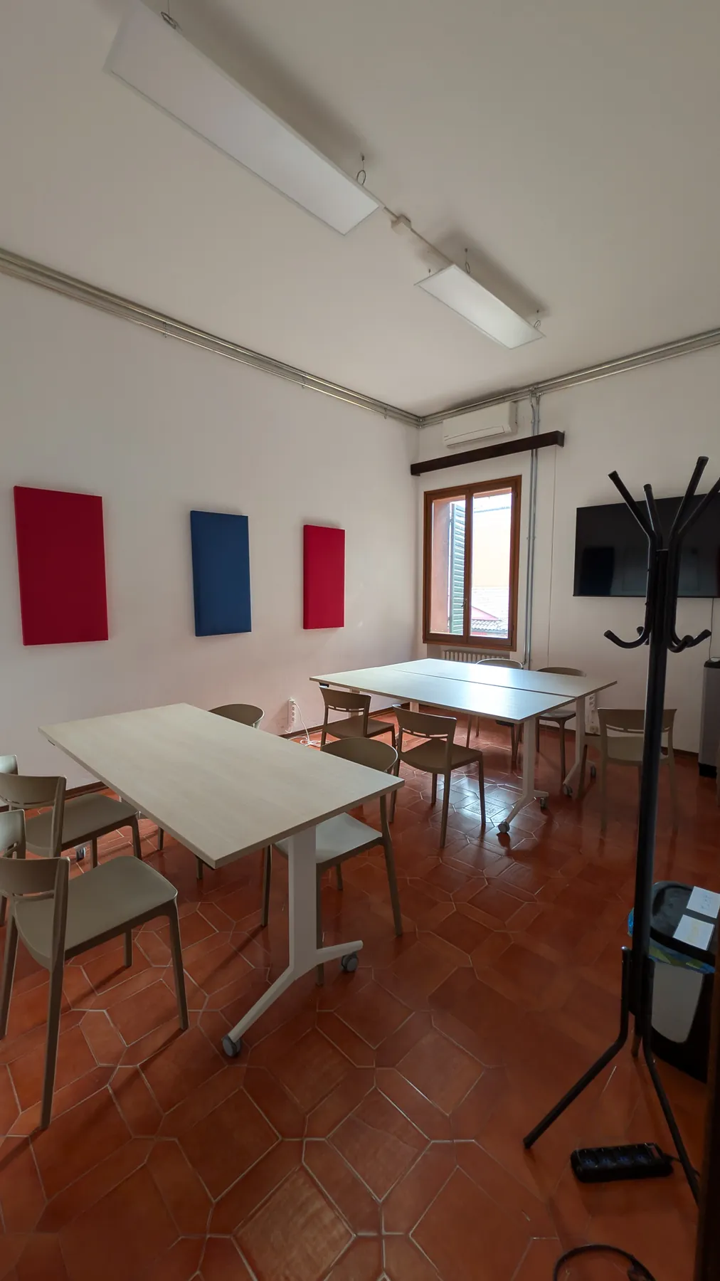Aula 3: pavimento in cotto, due tavoli, pannelli colorati alle pareti e una finestra.