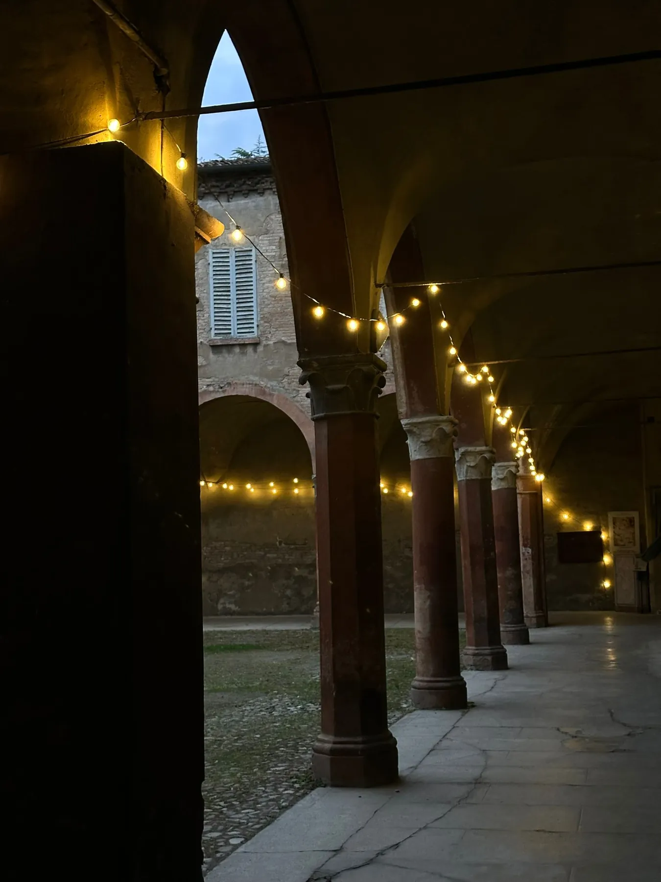 Il portico del chiostro la sera, con una fila di lucine accese tra le colonne.