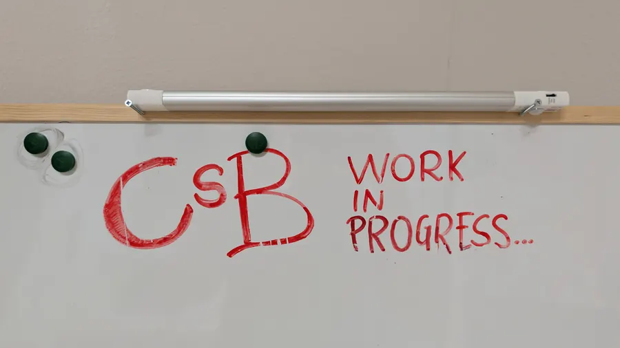 Una lavagna bianca con scritto a pennarello rosso: CsB work in progress.