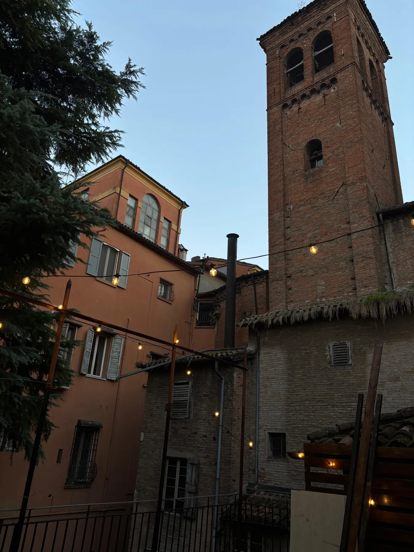 Il terrazzo al tramonto: il campanile di mattoni, i palazzi intorno e le lucine accese.